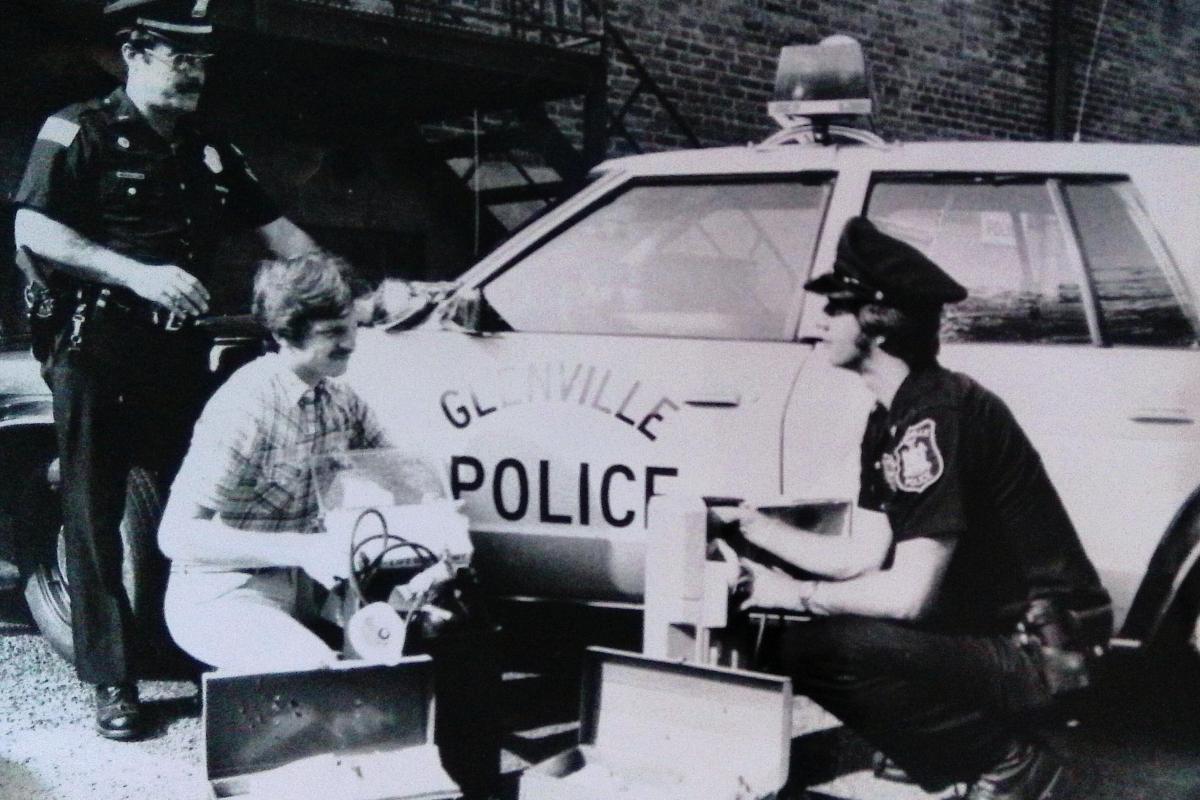 police officers crouching in front of a police car.