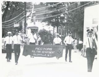 Firefighters march in a parade with a banner that reads "Rectors Volunteer Fire Department, Glenville, NY"
